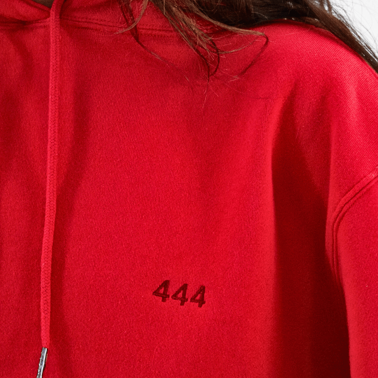A close-up of a person in a GFLApparel Angel Number 444 Hoodie, symbolizing a spiritual journey with the number "444" embroidered in black on the fabric.