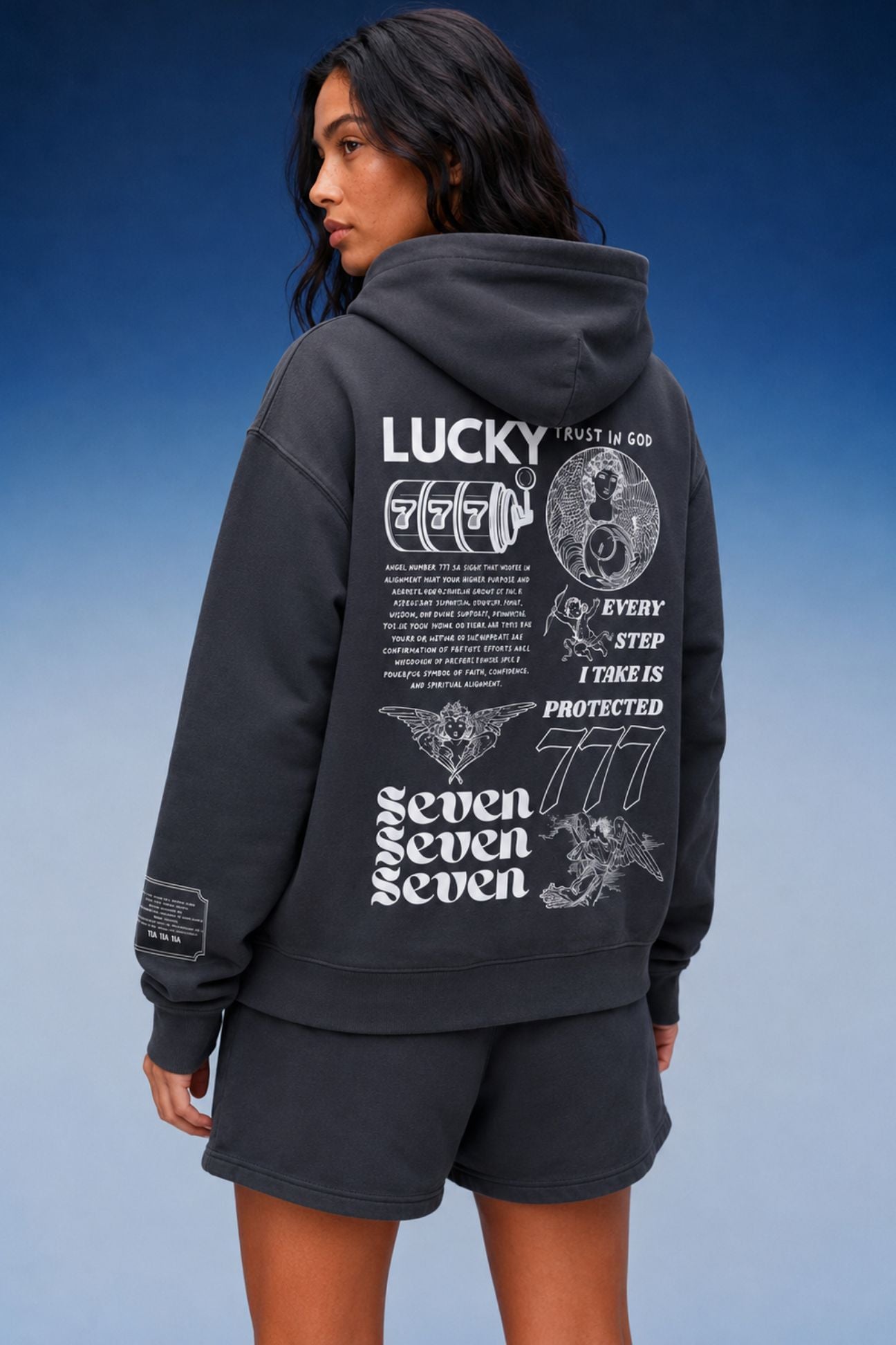 A model wearing an asteroid color hoodie and matching shorts, shown from the back. The hoodie features a large white graphic print on the back with the word 'LUCKY', 'SEVEN SEVEN SEVEN', and other illustrations.