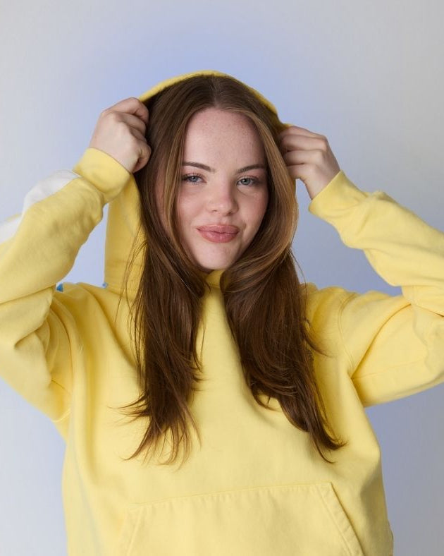 woman wearing yellow sweater surrounded by a light blue aura against a white wall