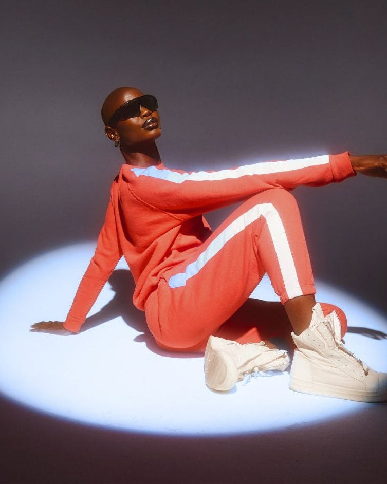 Person wearing a red tracksuit with reflective elements sitting on a dark background