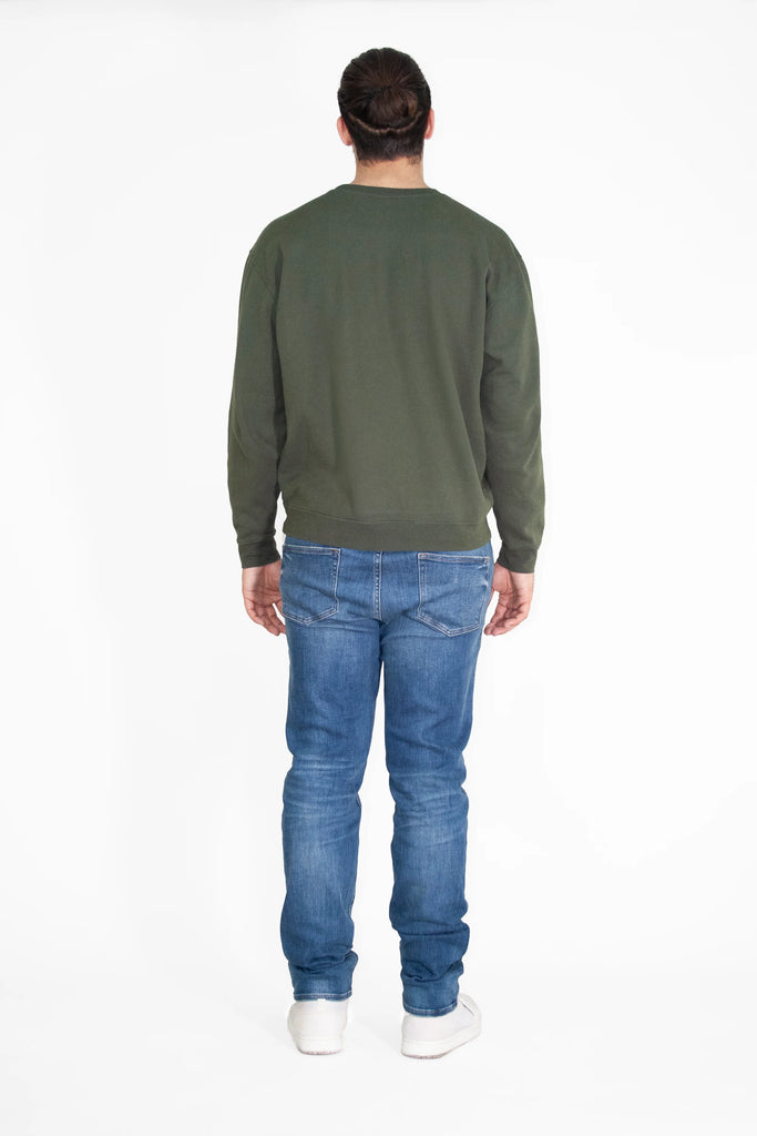The back view of a man wearing LIGHT WORKER CREWNECK IN CALADAN jeans and a green sweatshirt by GFLApparel.