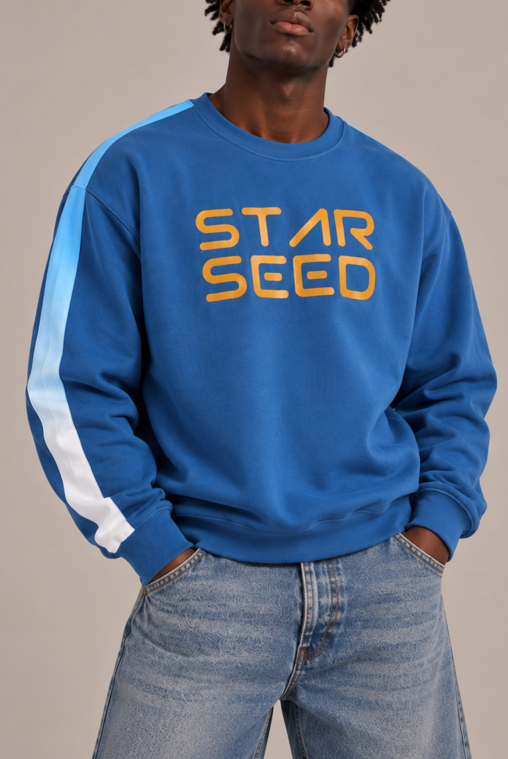 A man wearing a blue crewneck sweatshirt with 'STAR SEED' printed in orange across the chest, featuring a white and light blue stripe down the right sleeve, paired with light-wash blue jeans against a solid beige background.