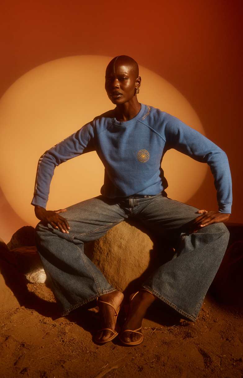 Person wearing a blue sweater and jeans sitting on a rock with a warm-toned background