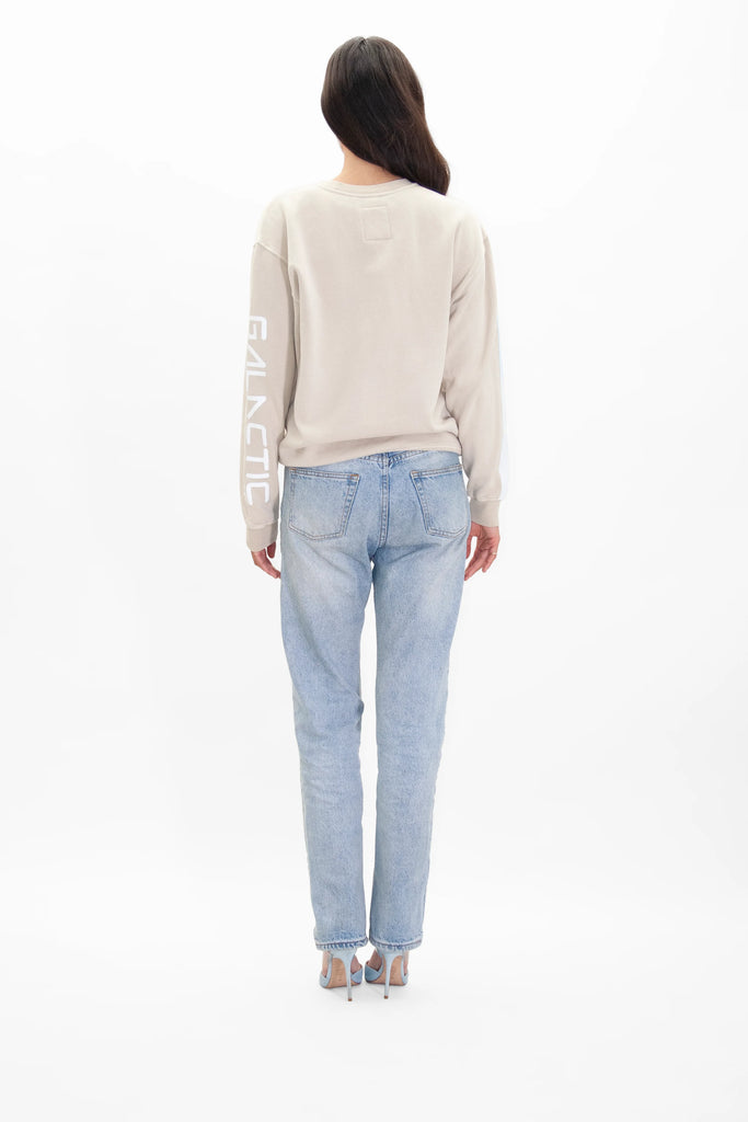 The back view of a woman wearing a GFLApparel MERKABA CREWNECK IN DUNE sweatshirt and jeans.