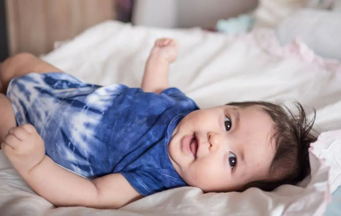 Indigo baby in tie-dye jumper smiles at the camera