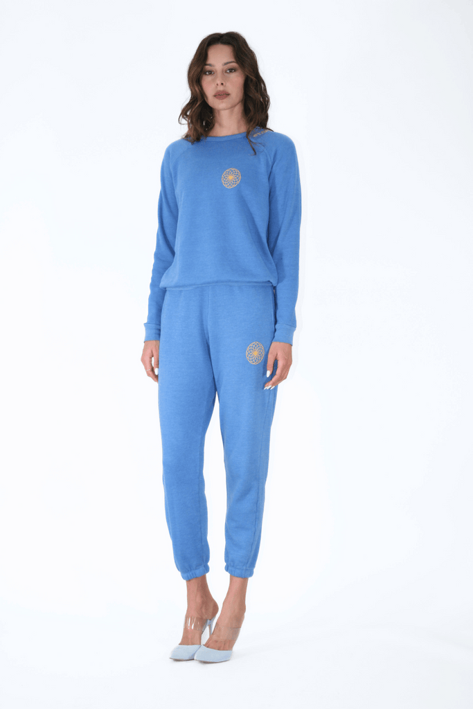 Woman posing in a blue tracksuit with Lotus spiritual symbolism, against a white background wearing Lotus of Life Women's Sweatpants by GFLApparel.
