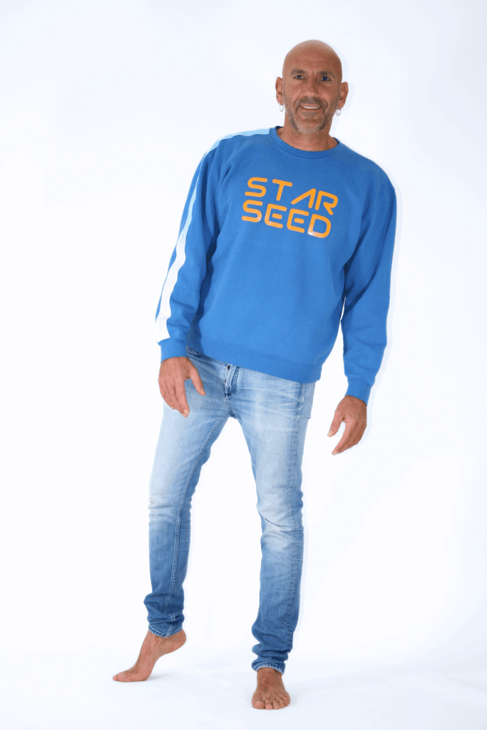 Man in blue GFLApparel Starseed Crewneck sweatshirt and jeans posing with hands on hips against a white background.