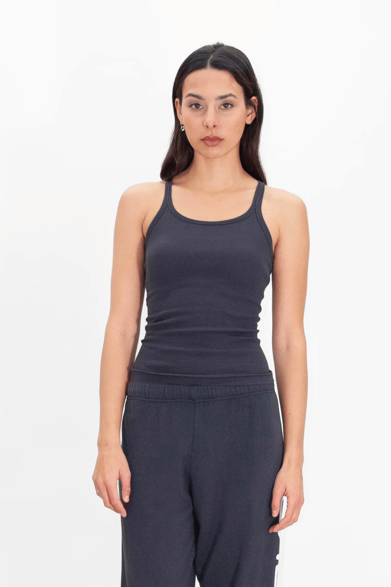 A woman standing against a white background, wearing a GFLApparel GFL Tank Top in Space Glow and navy sweatpants.