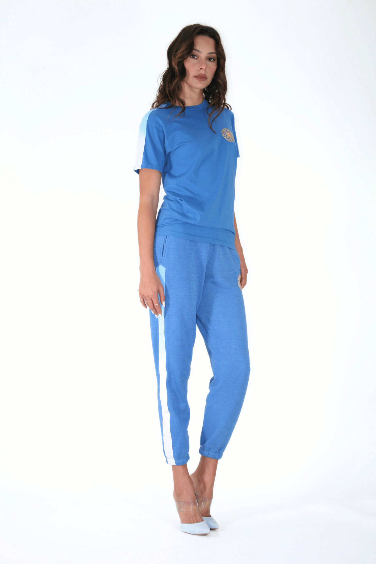 Woman posing in a blue tracksuit with white stripes, embodying the interconnectedness of sacred geometry, and Lotus of Life Tee by GFLApparel.