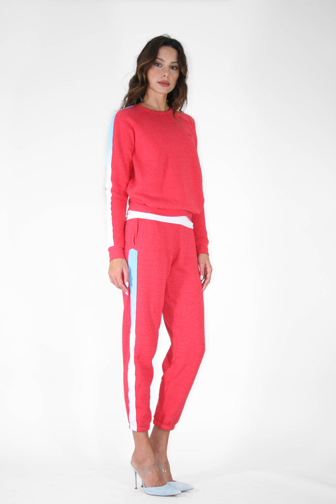 Woman posing in a red tracksuit with blue detailing and white heels, exuding an GFLApparel Angel Number 444 Women's Crewneck presence against a white background.