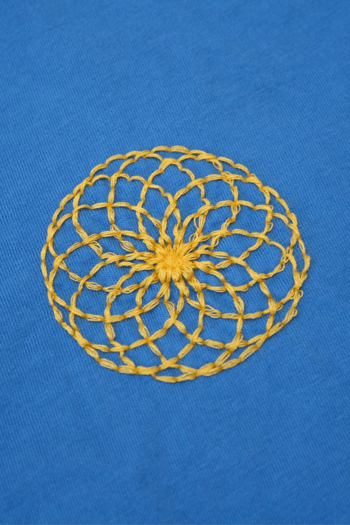 A yellow crocheted doily featuring the Lotus of Life Tee pattern on a blue fabric background by GFLApparel.