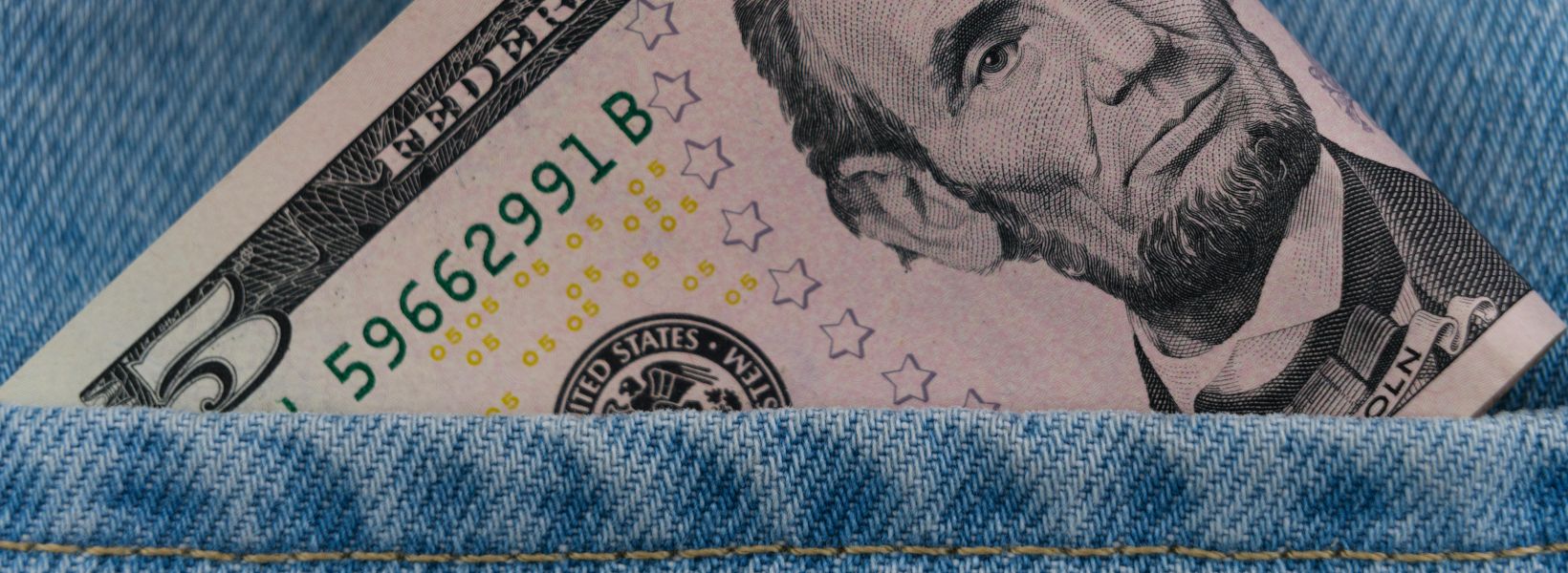 Five dollar bill peeking out from a blue denim pocket