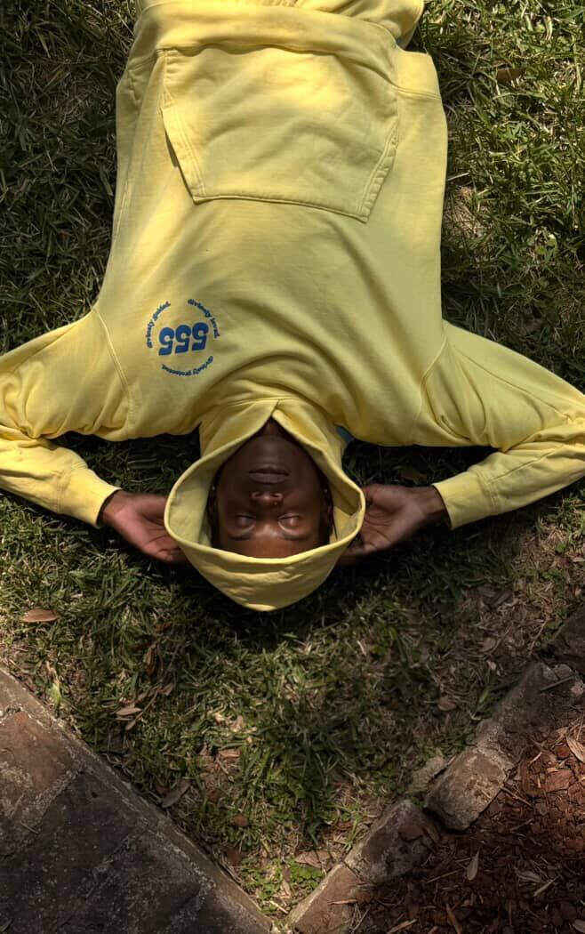 Person wearing a yellow hoodie with '555' logo lying on grass