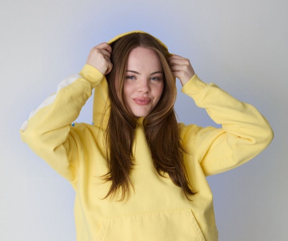 woman wearing yellow sweater surrounded by a light blue aura against a white wall