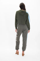 A person stands facing away, wearing a GFLApparel Light Worker Cropped Hoodie in Caladan, matching jogger pants with white lettering on the side, and beige heeled sandals.
