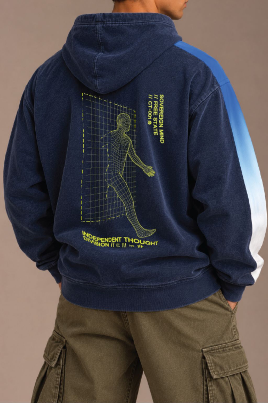 A person shown from the back wearing a navy hoodie with a large yellow graphic saying INDEPENDENT THOUGHT DIVISION print on the back and blue-to-white color-blocked sleeves, paired with olive cargo pants against a plain beige studio background.