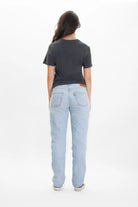 A person wearing a dark grey GFL Stack Tee in Space Glow from GFLApparel and light blue jeans, standing and facing away from the camera against a plain white background.
