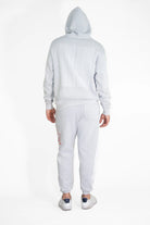 Back view of a person wearing a light gray Hypergalactic Hoodie in Galactic Gray by GFLApparel, made from a heavyweight cotton blend, with the hood pulled up, white shoes, and graphics on the back of the handcrafted in LA hoodie and the side of the pants.