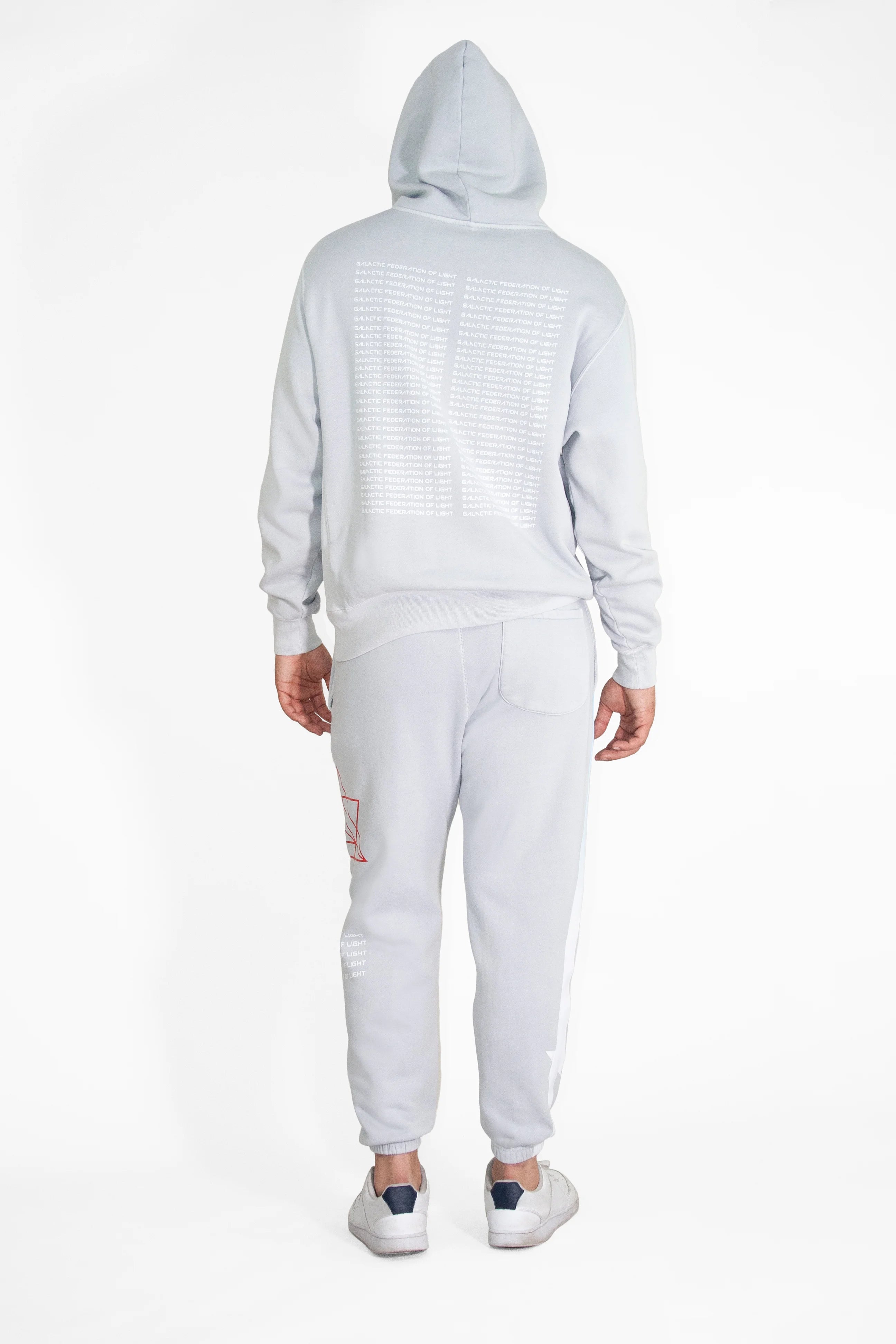 Back view of a person wearing a light gray Hypergalactic Hoodie in Galactic Gray by GFLApparel, made from a heavyweight cotton blend, with the hood pulled up, white shoes, and graphics on the back of the handcrafted in LA hoodie and the side of the pants.