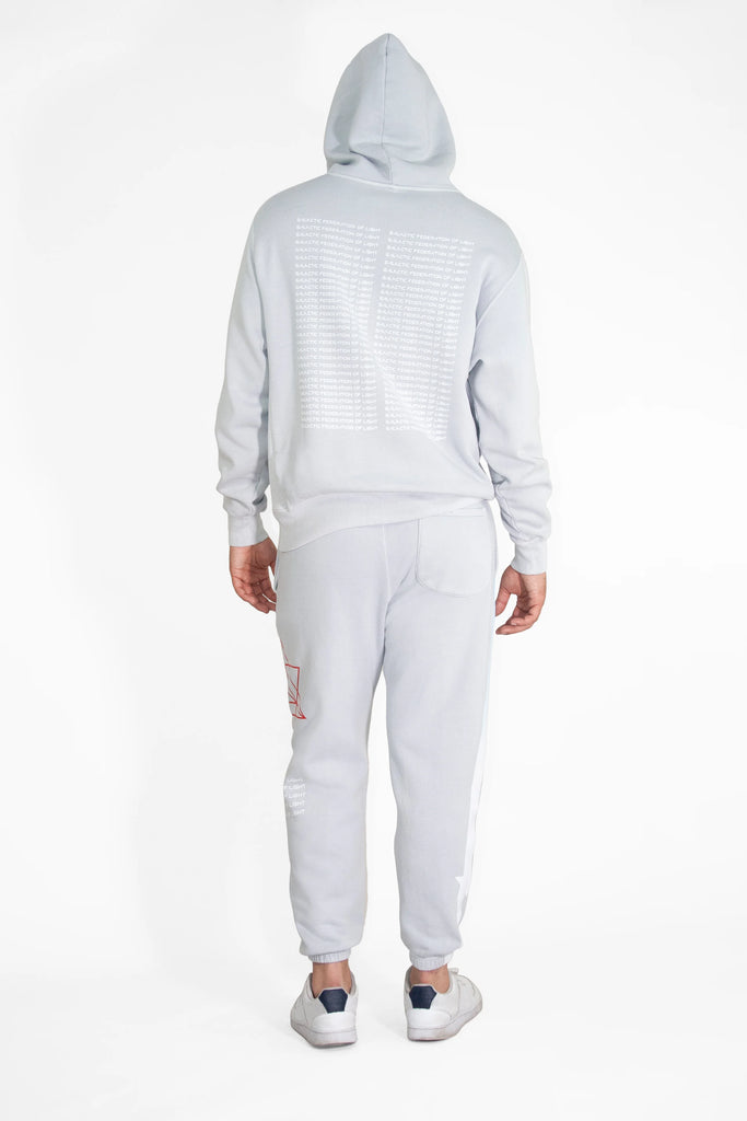 Back view of a person wearing a light gray Hypergalactic Hoodie in Galactic Gray by GFLApparel, made from a heavyweight cotton blend, with the hood pulled up, white shoes, and graphics on the back of the handcrafted in LA hoodie and the side of the pants.