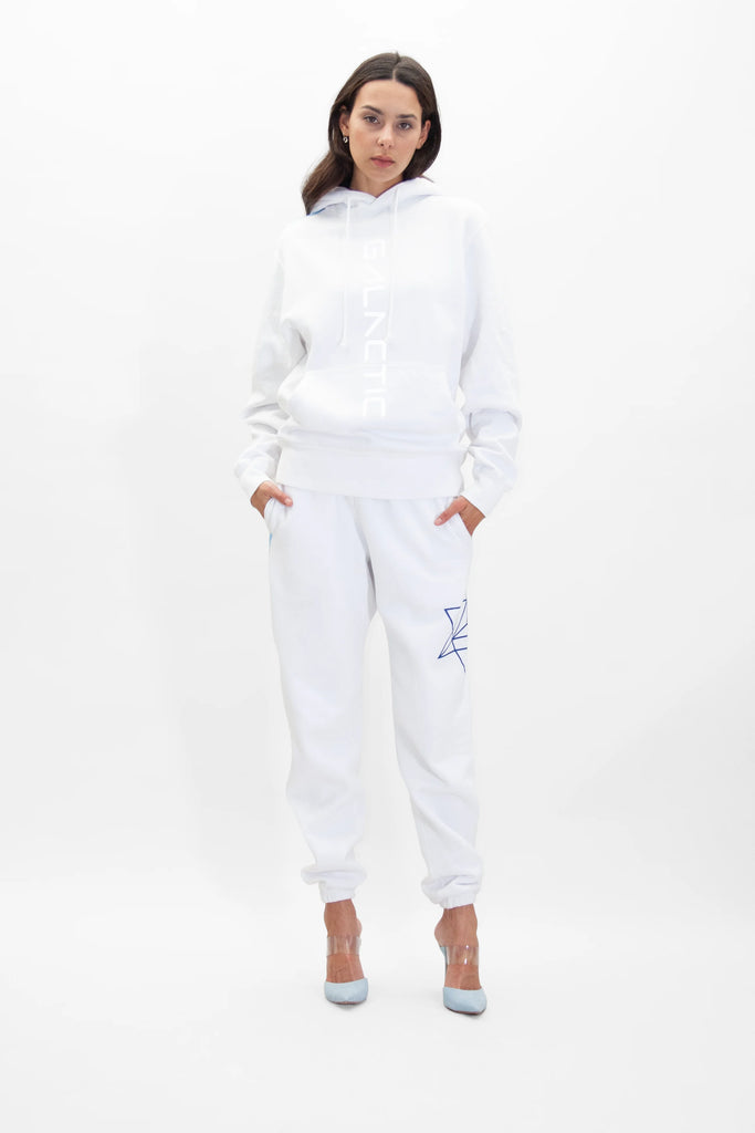 Person wearing a GFLApparel Hypergalactic Hoodie in Lite Beam, matching heavyweight cotton blend white sweatpants with a blue star design on the left thigh, and clear high-heeled shoes, standing against a plain white background.