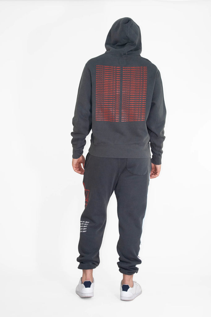 A person is standing with their back to the camera, wearing a GFLApparel Hypergalactic Hoodie in Space Glow and matching sweatpants handcrafted in LA, both made from a heavyweight cotton blend. The hoodie features red text, the pants white text, and they complete the look with white sneakers.
