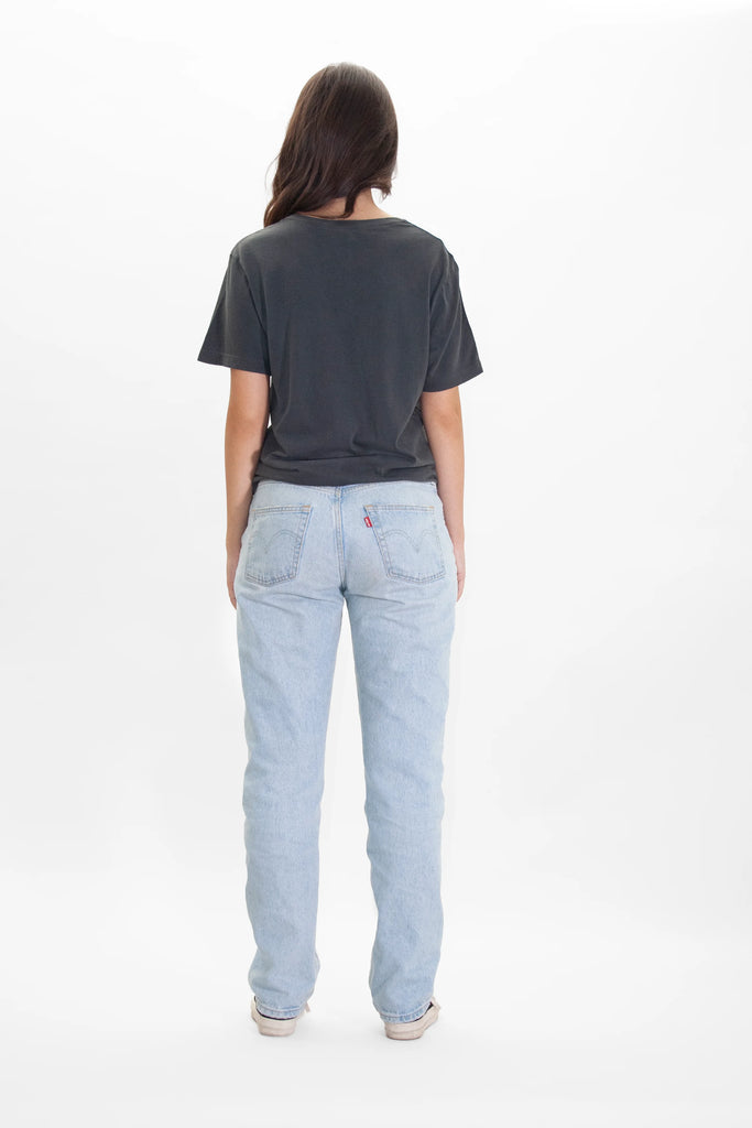 The back view of a woman wearing GFLApparel's ILLUMINATED TEE IN SPACE GLOW jeans.