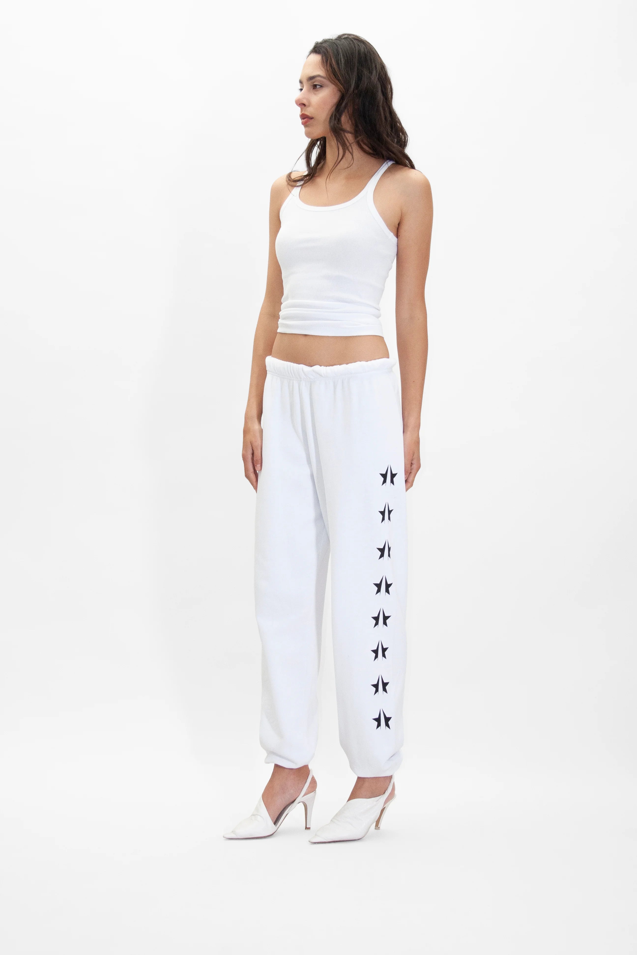 A woman wearing white sweatpants and a GFL Tank Top in Lite Beam by GFLApparel.