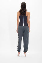 Back view of a person with long dark hair wearing a black tank top, GFLApparel GFL Stars Sweatpants in Space Glow, and white high heels, standing against a plain white background.