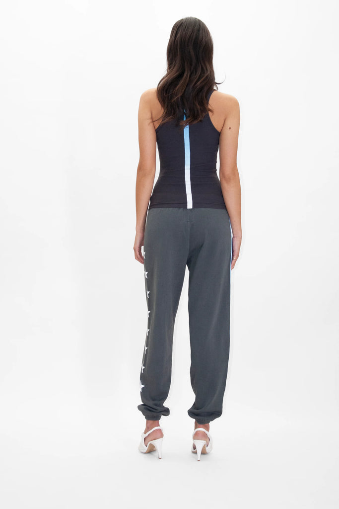 Back view of a person with long dark hair wearing a black tank top, GFLApparel GFL Stars Sweatpants in Space Glow, and white high heels, standing against a plain white background.