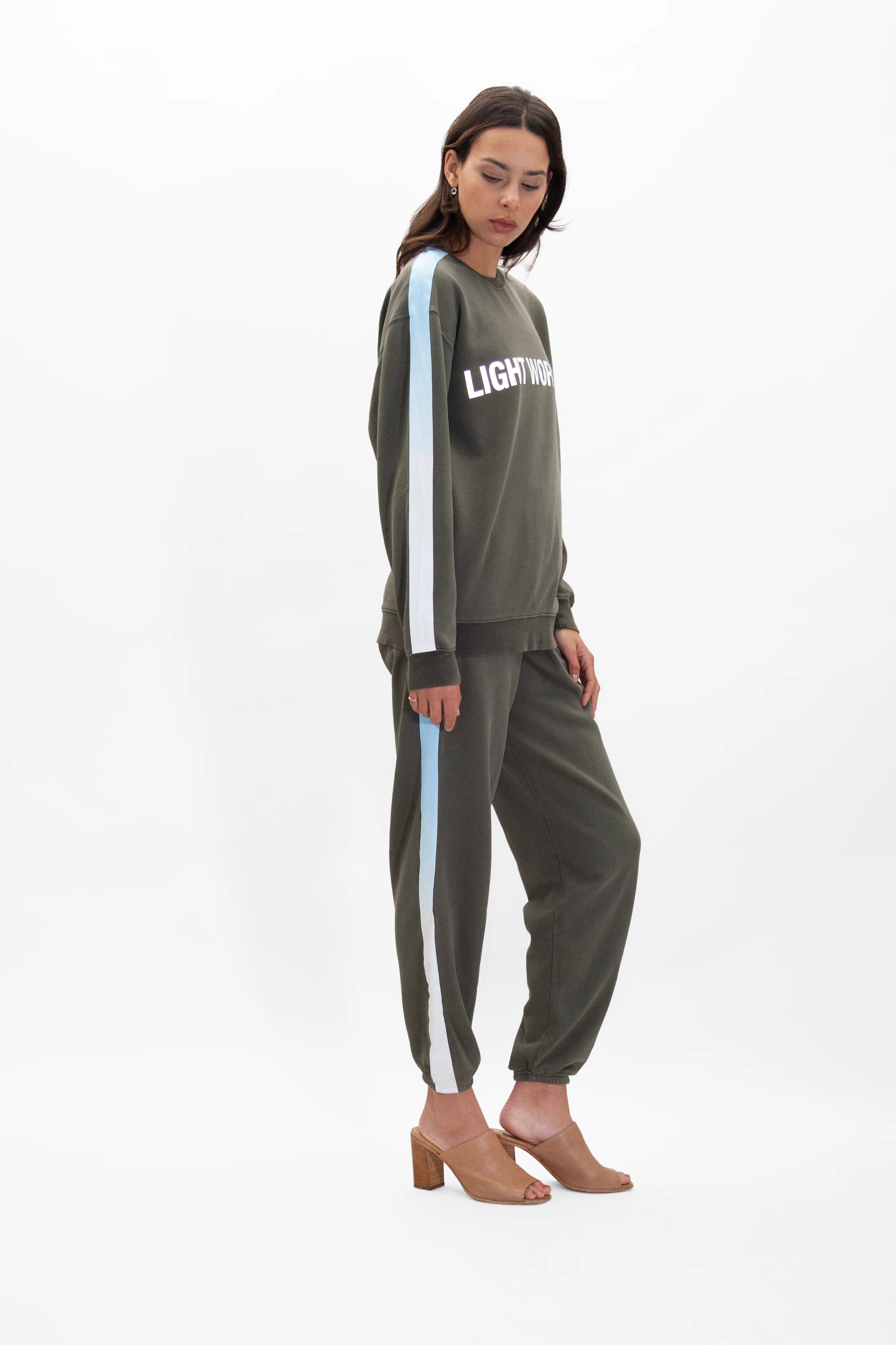 A person wearing a dark sweatshirt with the word "LIGHTWORK" on the chest, paired with matching Galactic Sweatpants in Caladan by GFLApparel that have light blue and white stripes down the sides, and tan heeled shoes.