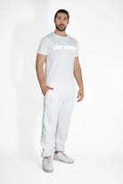 Man standing against a white background wearing a white T-shirt that says "LIGHT WORKER" in reflective print, white pants, and white sneakers, with his left hand in his pocket. The Light Worker Tee in Lite Beam by GFLApparel is crafted from soft, breathable cotton for all-day comfort.