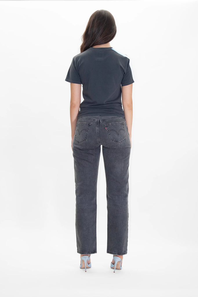 The back view of a woman wearing grey jeans and a GFLApparel LIGHT WORKER TEE IN SPACE GLOW.