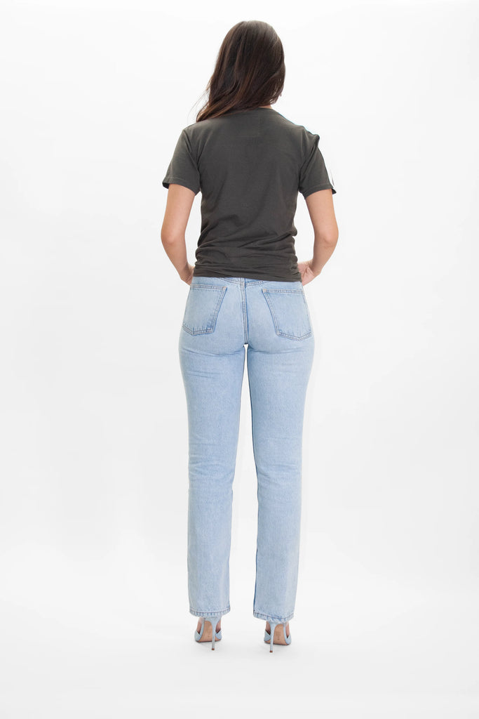 A person with long dark hair wearing a reflective print dark Light Worker Tee in Caladan by GFLApparel, light blue jeans, and high heels is standing facing away from the camera.
