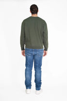 A person with long hair in a bun is standing with their back facing the camera, wearing a GFLApparel Light Worker Crewneck in Caladan, blue jeans, and white shoes against a plain white background.