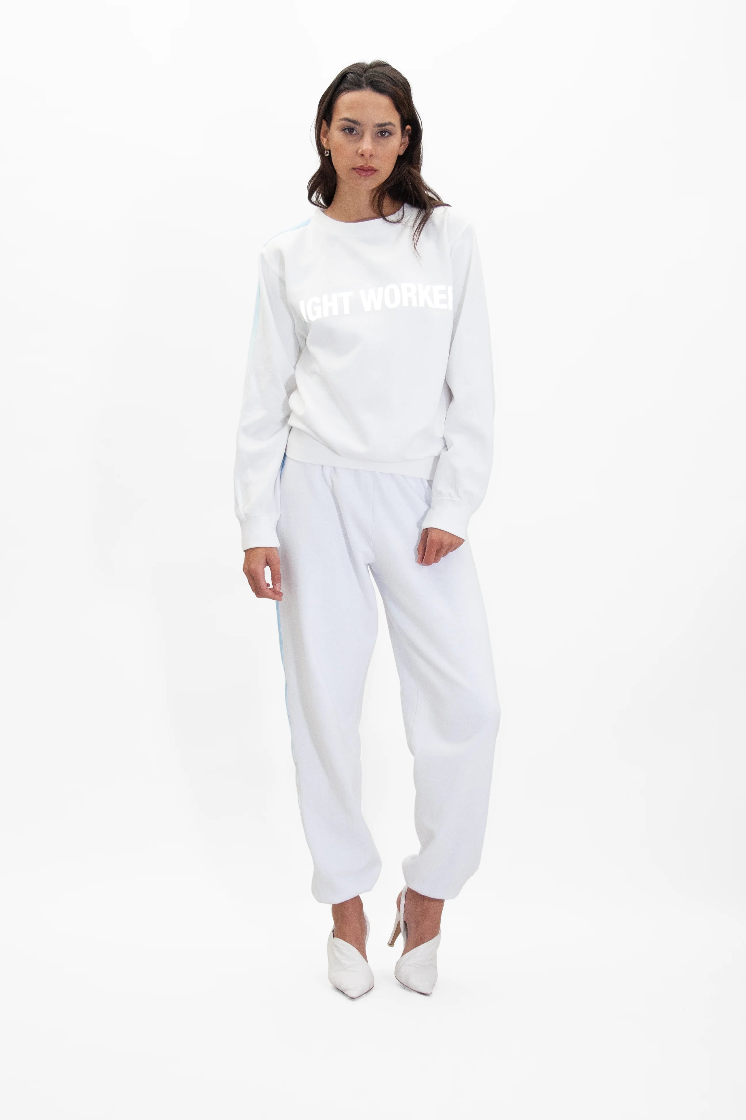 Person wearing a white Light Worker Crewneck in Lite Beam from GFLApparel with the text "LIGHT WORKER" in reflective print and matching white sweatpants, standing against a plain white background.