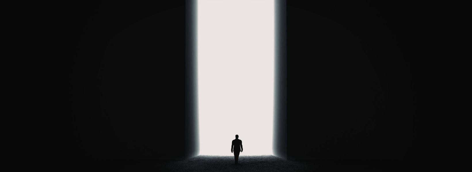 Person standing at the threshold of a bright light in a dark setting