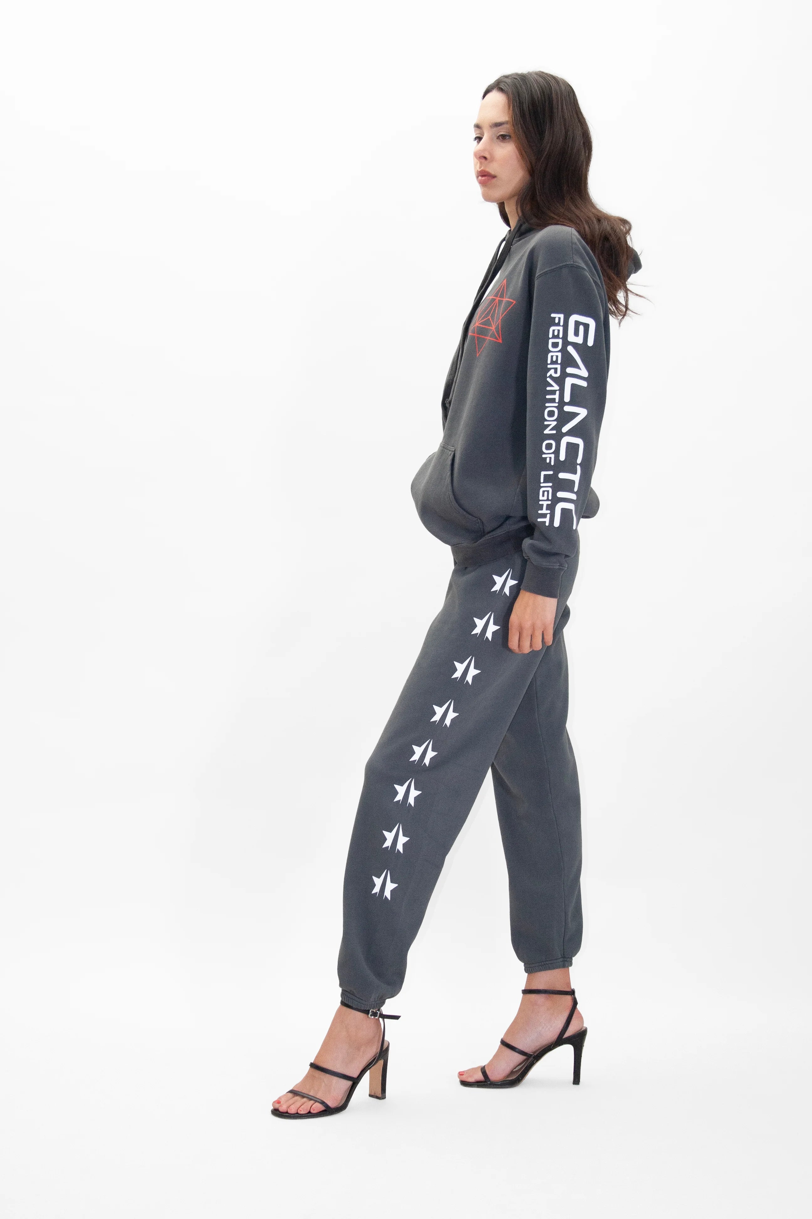 Woman in a Merkaba Hoodie in Space Glow by GFLApparel, and matching joggers adorned with white star patterns and text 