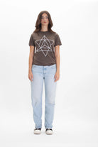 A person is standing against a white background, wearing a GFLApparel Merkaba Tee in Earth featuring sacred geometry with a geometric design, light blue jeans, and white sneakers.