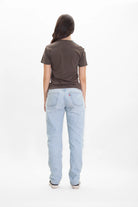 Person standing with their back to the camera wearing a Merkaba Tee in Earth by GFLApparel, light blue jeans, and white shoes, reminiscent of sacred geometry in its simplicity.