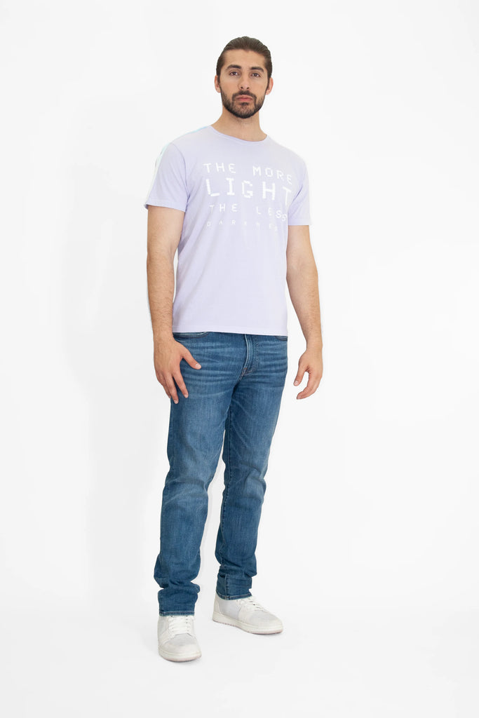 A man wearing a MORE LIGHT TEE IN NEBULA t - shirt by GFLApparel and jeans.