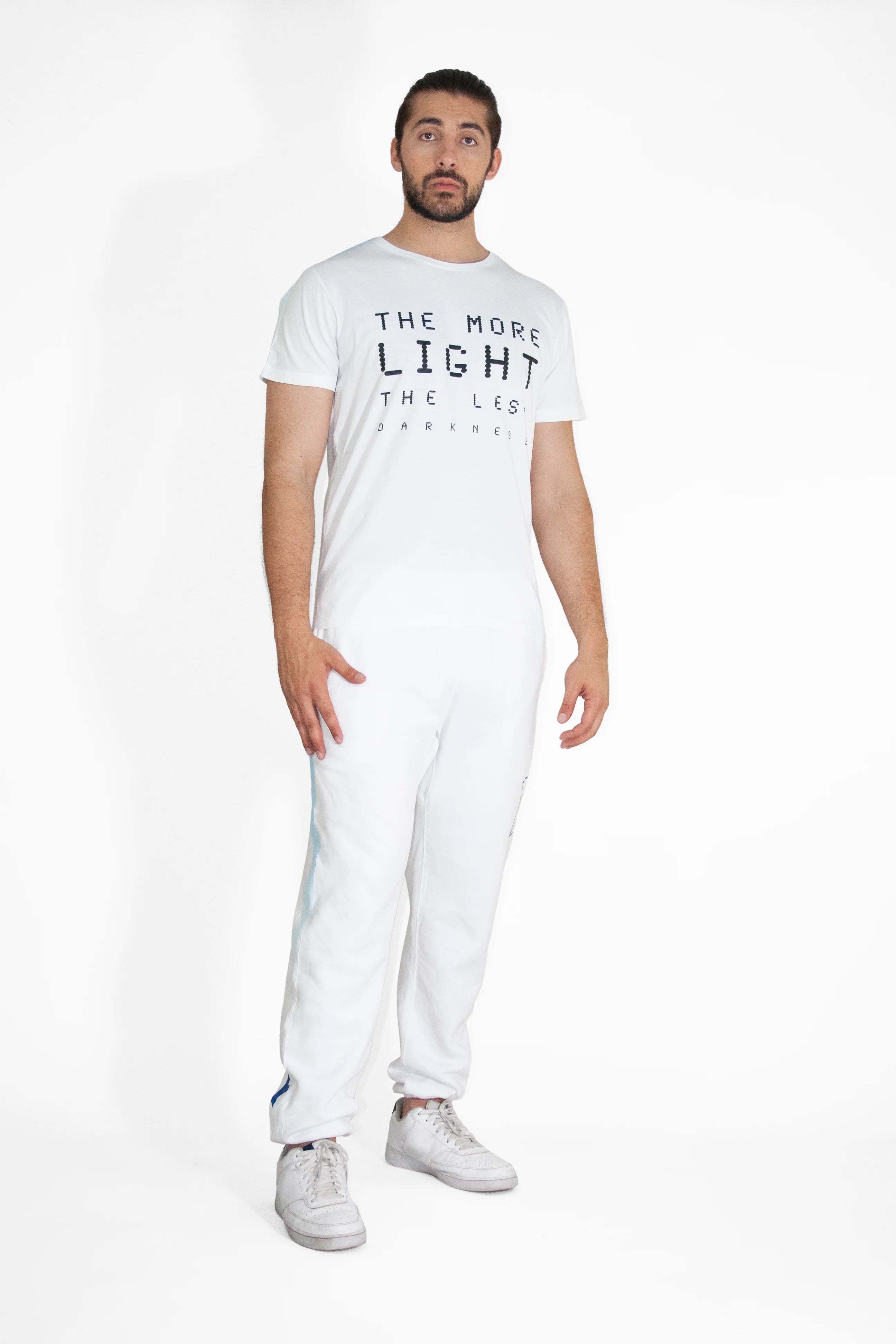A man stands against a plain white background, wearing a GFLApparel More Light Tee in Lite Beam with the phrase 