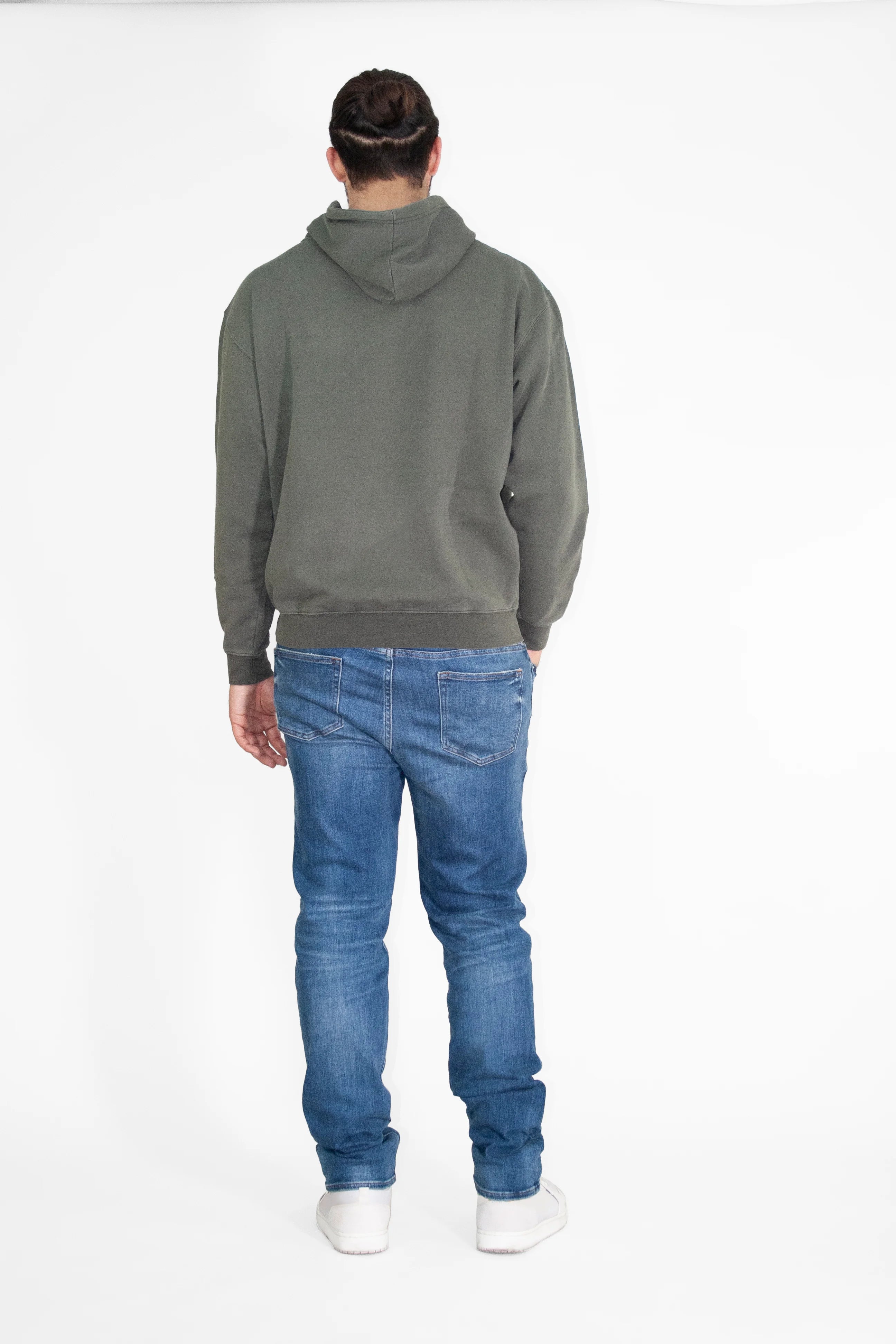 A person standing with their back to the camera, wearing a green GFLApparel GFL Stars Hoodie in Caladan, blue jeans, and white shoes against a white background.