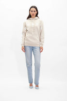 A person stands against a white background wearing a light beige GFLApparel GFL Stars Hoodie in Dune with white star designs, light blue jeans, and matching light blue shoes.