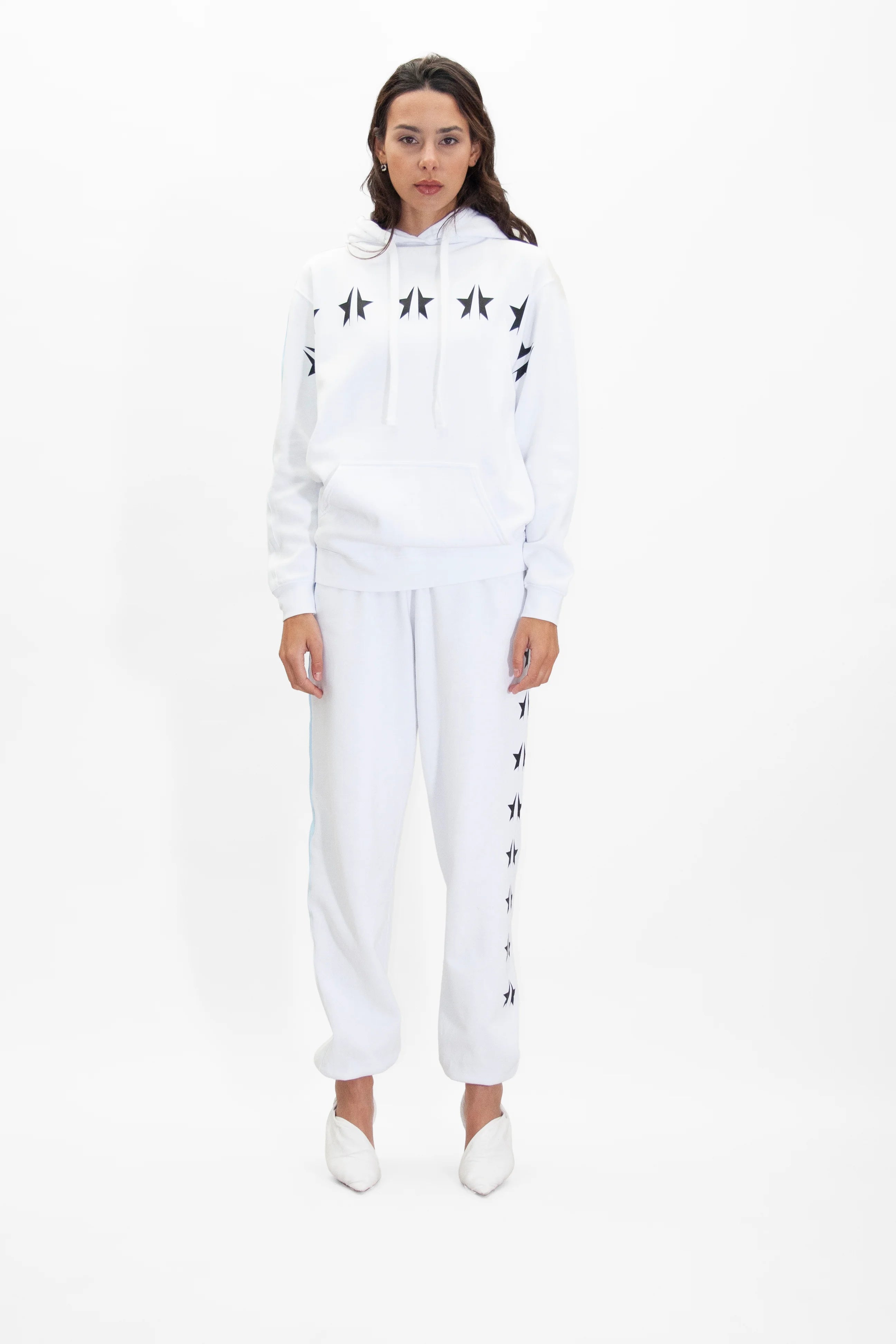 A person stands against a plain background, wearing an all-white GFLApparel GFL Stars Hoodie in Lite Beam made from soft breathable cotton and matching white sweatpants. They are also wearing white shoes.
