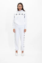 A person stands against a plain background, wearing an all-white GFLApparel GFL Stars Hoodie in Lite Beam made from soft breathable cotton and matching white sweatpants. They are also wearing white shoes.