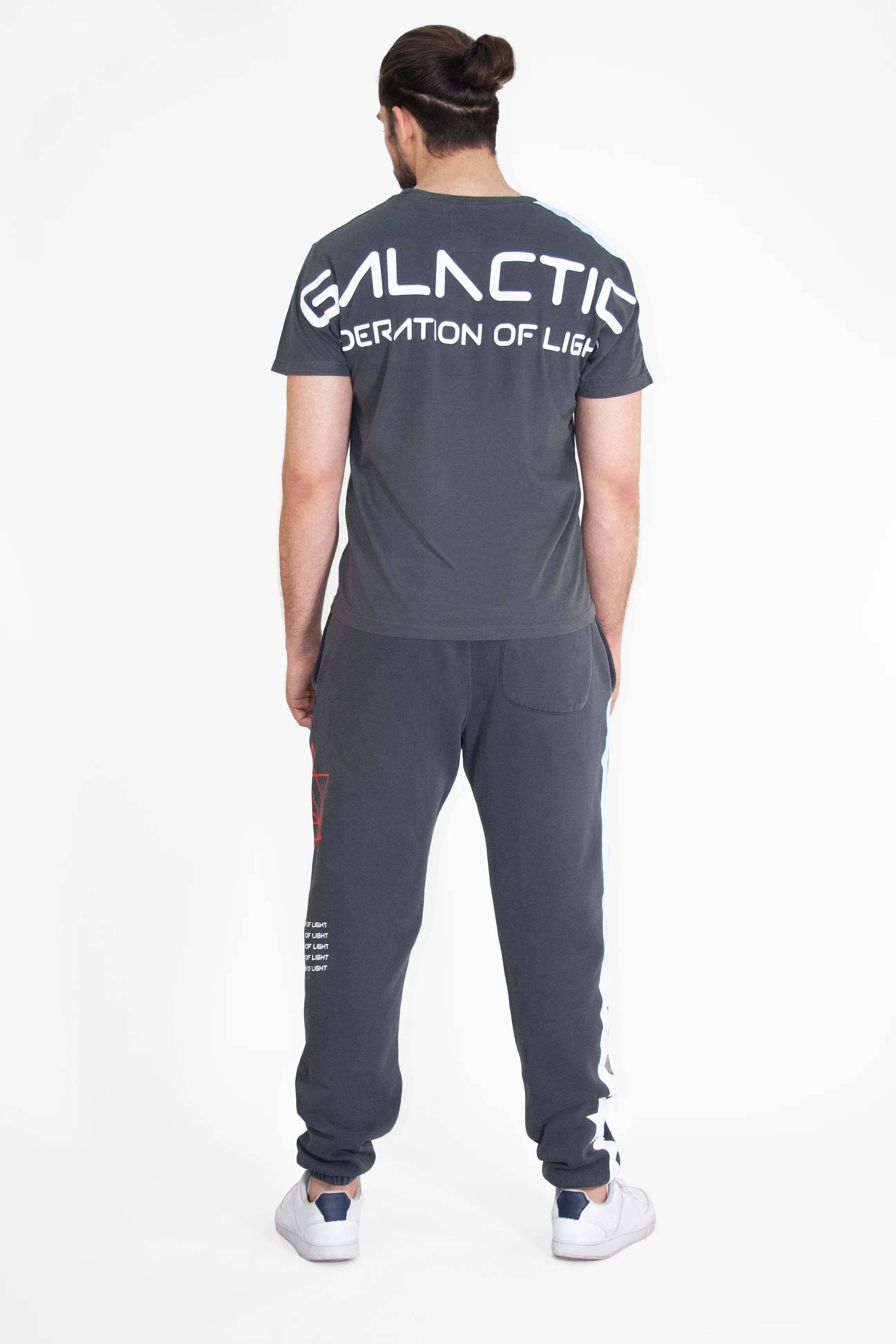 A person with a bun stands facing away, wearing a dark gray GFLApparel GFL Stars Tee in Space Glow with 