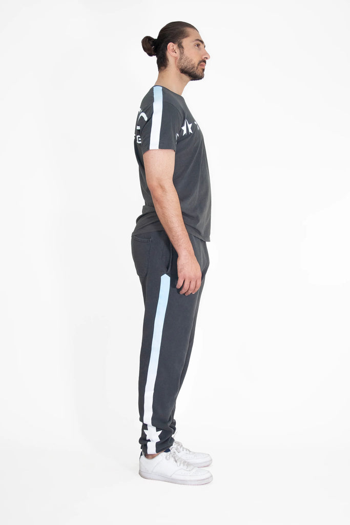 A man is standing in front of a white background in a GFLApparel STARS TEE IN SPACE GLOW tracksuit.