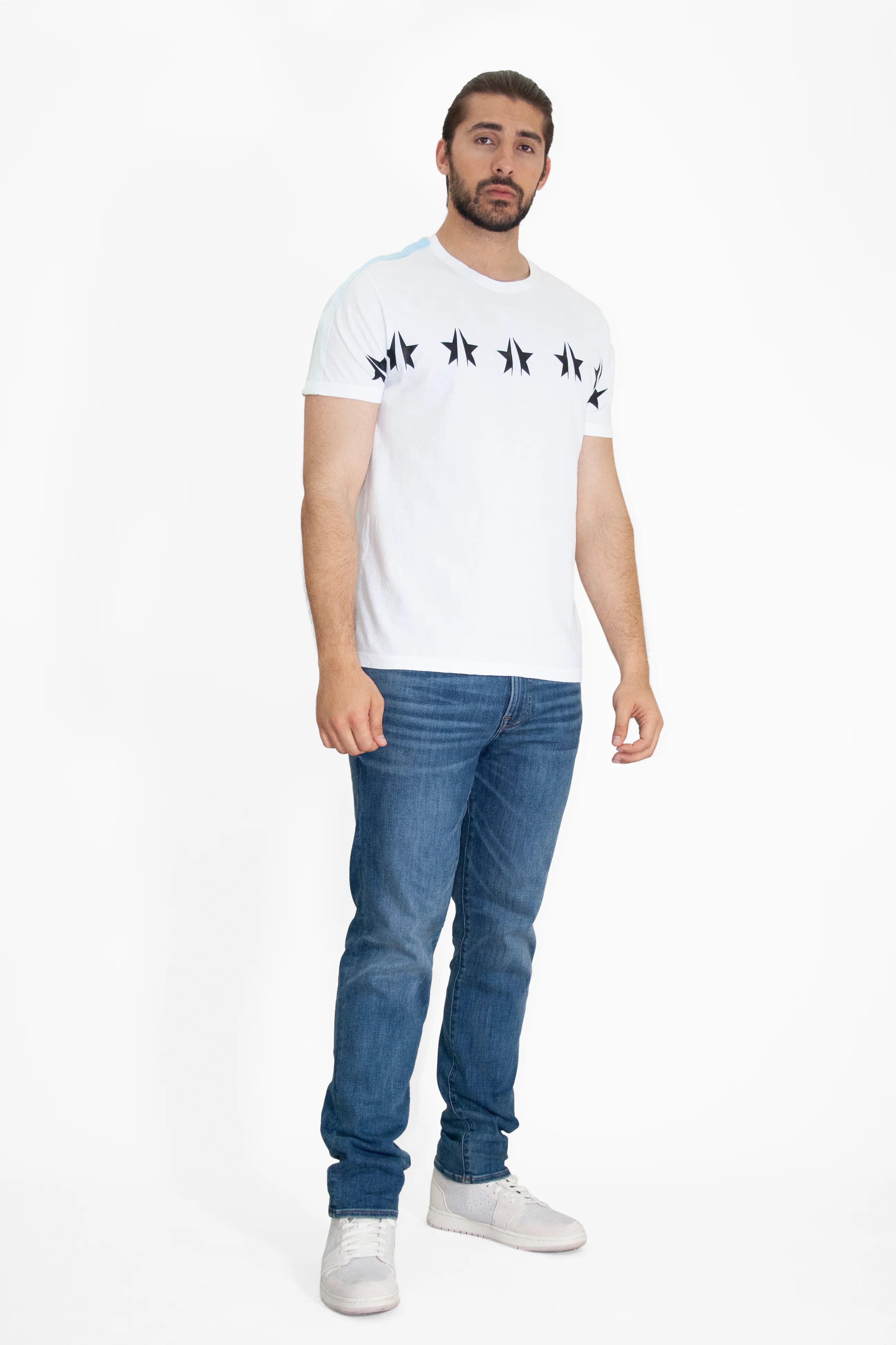 A man with a beard, wearing a GFLApparel GFL Stars Tee in Lite Beam made from breathable cotton, blue jeans in a relaxed fit, and white shoes, stands against a plain white background.