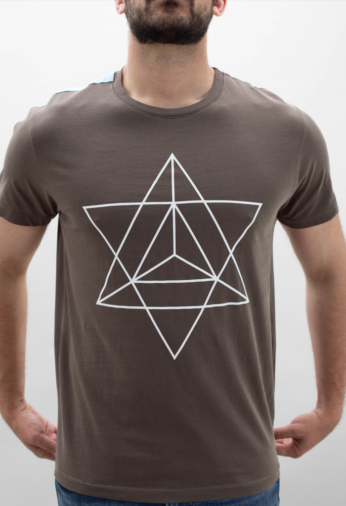 A man wearing the GFLApparel Merkaba Tee in Earth, with a geometric star design reminiscent of the Merkaba symbol from sacred geometry, stands against a plain white background.